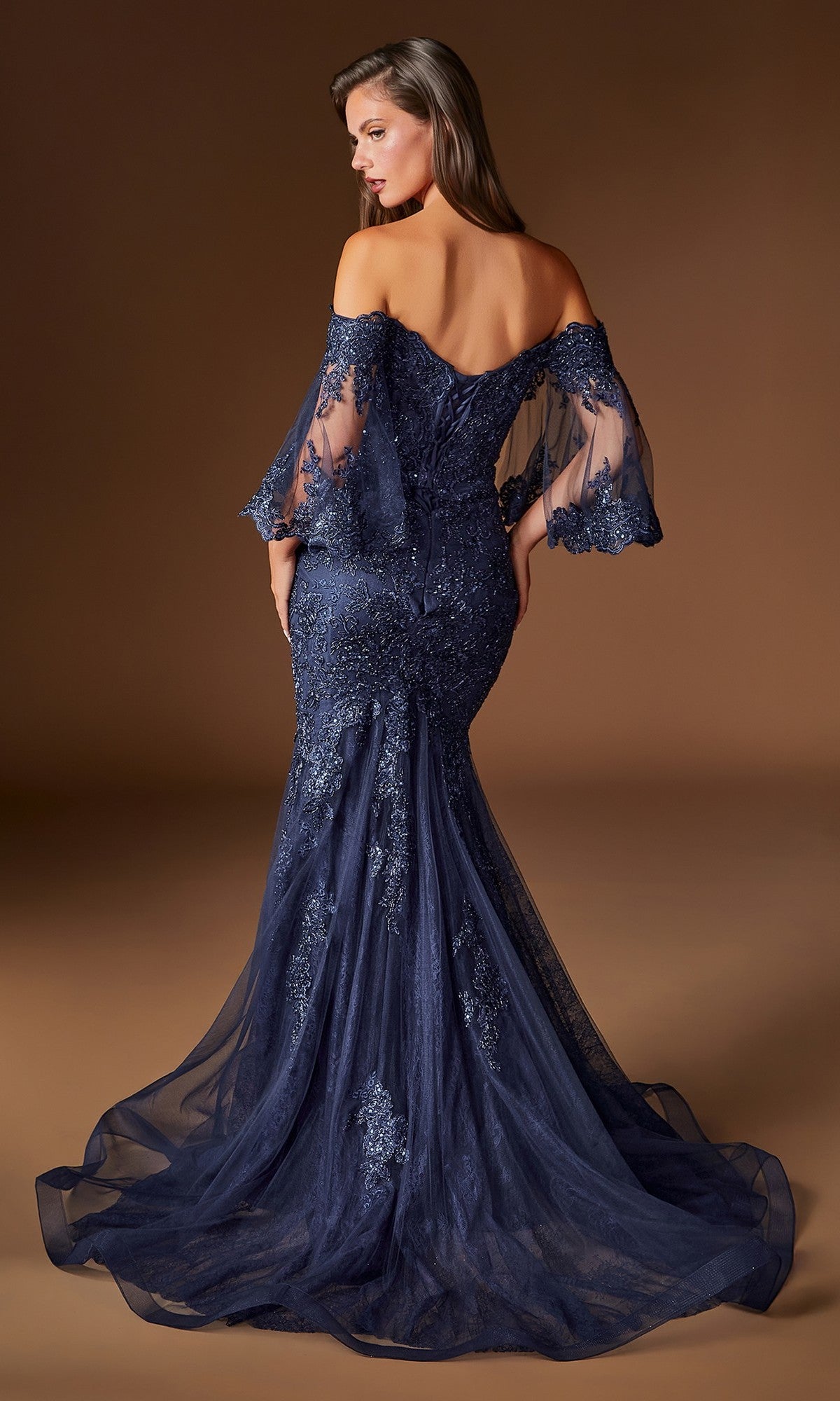 A woman is photographed from the back against a brown background wearing the Ladivine CD659, a long navy blue formal dress with an off-shoulder embellished bodice, lace details, and a flowing train that exudes elegance and sophistication.